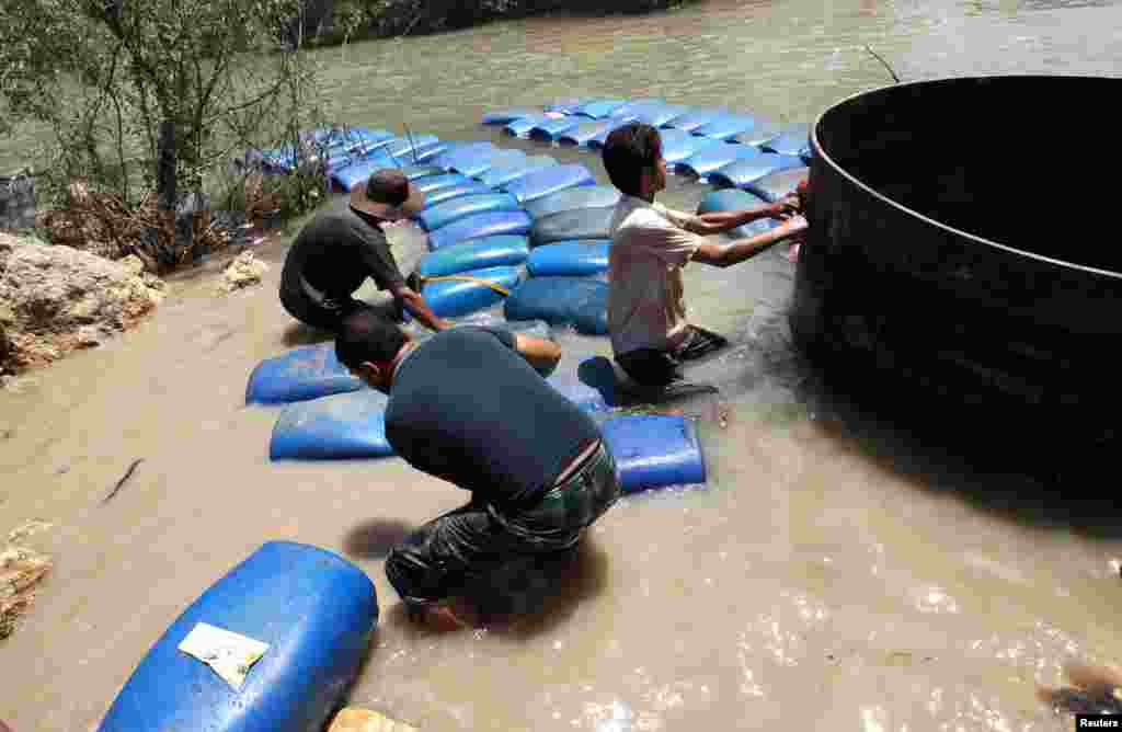 A group of men smuggle diesel fuel from Syria to Turkey hoping to sell it at a higher price, across the Al-Assi River in Idlib, May 26, 2013.